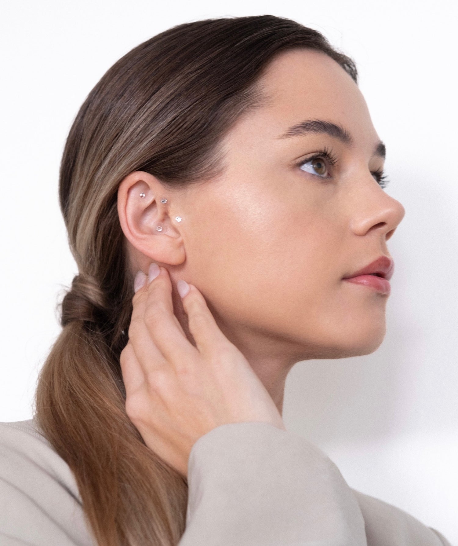 An image of a woman facing right with a ponytail. The woman is holding her neck, showing elegance.