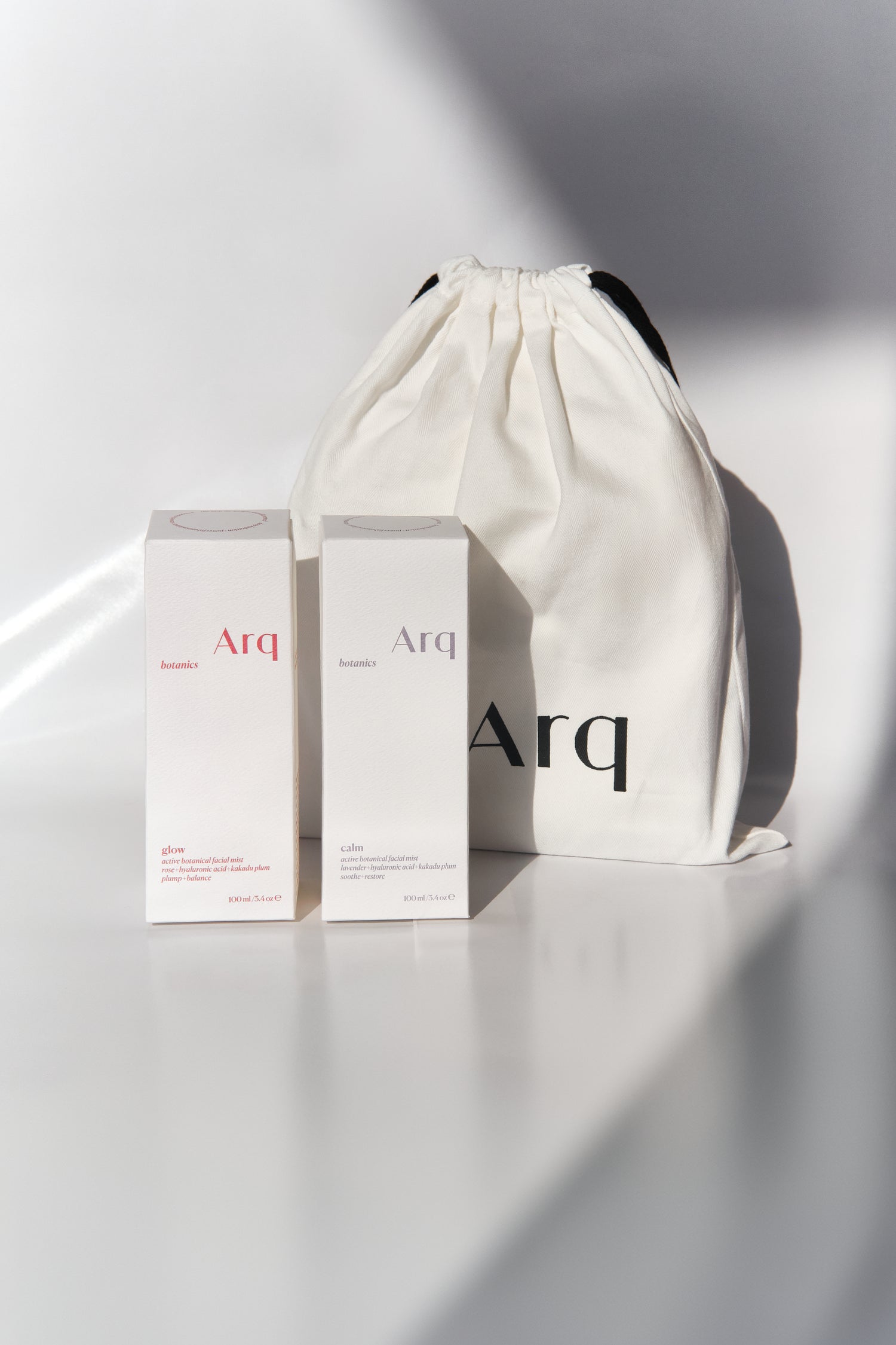 Two white boxes with the "Arq" logo, one labeled "Glow" and the other "Calm." Both are next to a white drawstring pouch with the "Arq" logo.