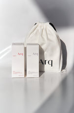 Two white boxes with the "Arq" logo, one labeled "Glow" and the other "Calm." Both are next to a white drawstring pouch with the "Arq" logo.