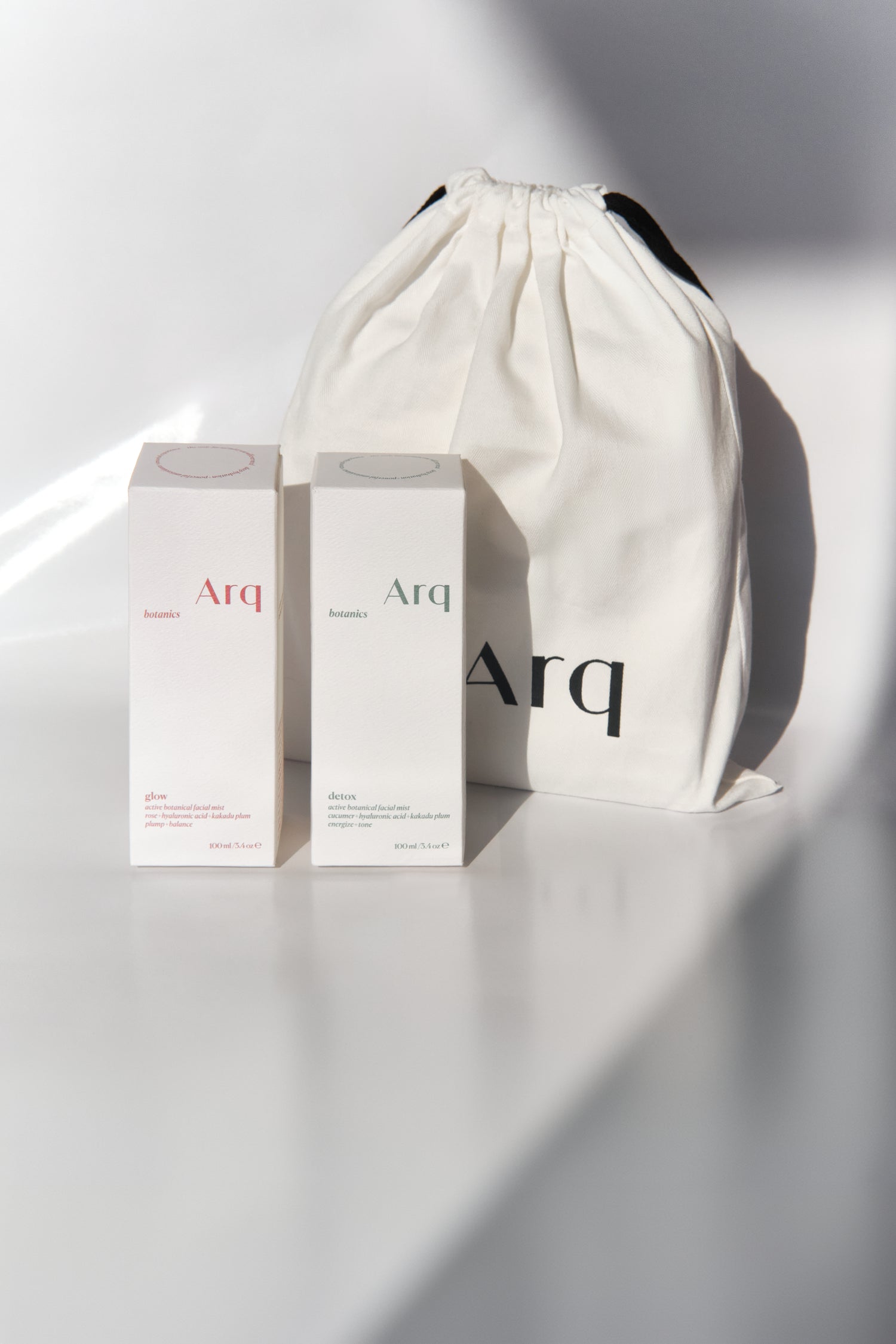 Two white boxes with the "Arq" logo, one labeled "Glow" and the other "Detox." Both are next to a white drawstring pouch with the "Arq" logo.