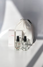 Two clear glass bottles of Arq Botanics Glow Hyaluronic Acid Facial Mist with black spray pumps, next to a white drawstring pouch.