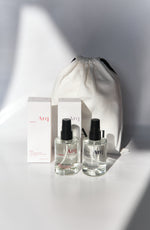 Two clear glass bottles of Arq Botanics Glow Hyaluronic Acid Facial Mist with black spray pumps, next to a white drawstring pouch.